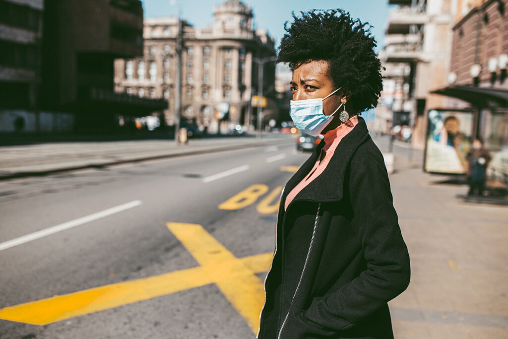 Young African American woman standing on city street with protective mask on her face.
