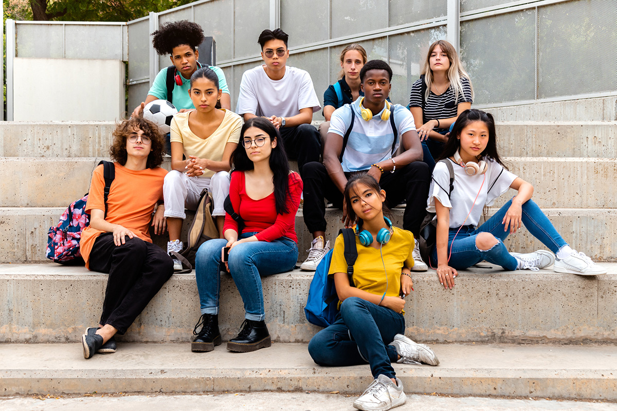 Multiracial teenage students sitting on steps in high school outside looking at camera with serious expression